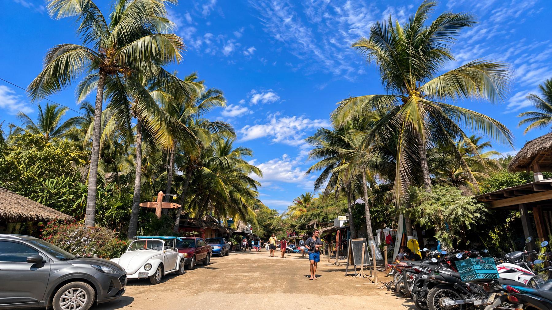 Calle de Zicatela en Puerto Escondido con palmeras, autos y motos